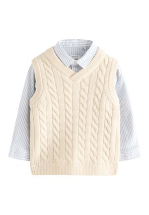 Cream cable-knit sleeveless sweater vest layered over a light blue and white striped collared long-sleeve shirt.