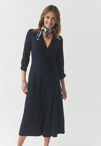 Navy wrap dress made of soft fabric features a V-neckline, three-quarter sleeves, a side knot detail, and a flowing A-line skirt.