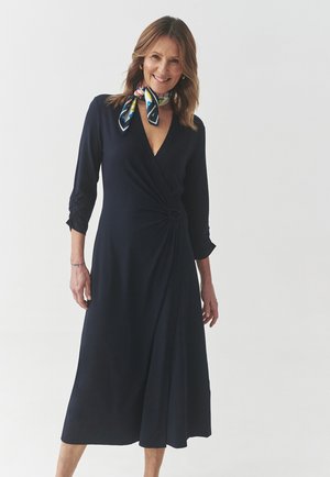 Navy wrap dress made of soft fabric features a V-neckline, three-quarter sleeves, a side knot detail, and a flowing A-line skirt.