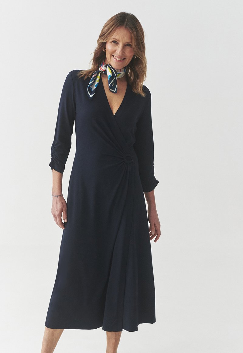 Navy wrap dress made of soft fabric features a V-neckline, three-quarter sleeves, a side knot detail, and a flowing A-line skirt.