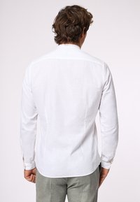 Camicia bianca di lino con vestibilità aderente, maniche lunghe, polsini con bottone e orlo curvo. Design minimalista, texture liscia e tessuto leggero.