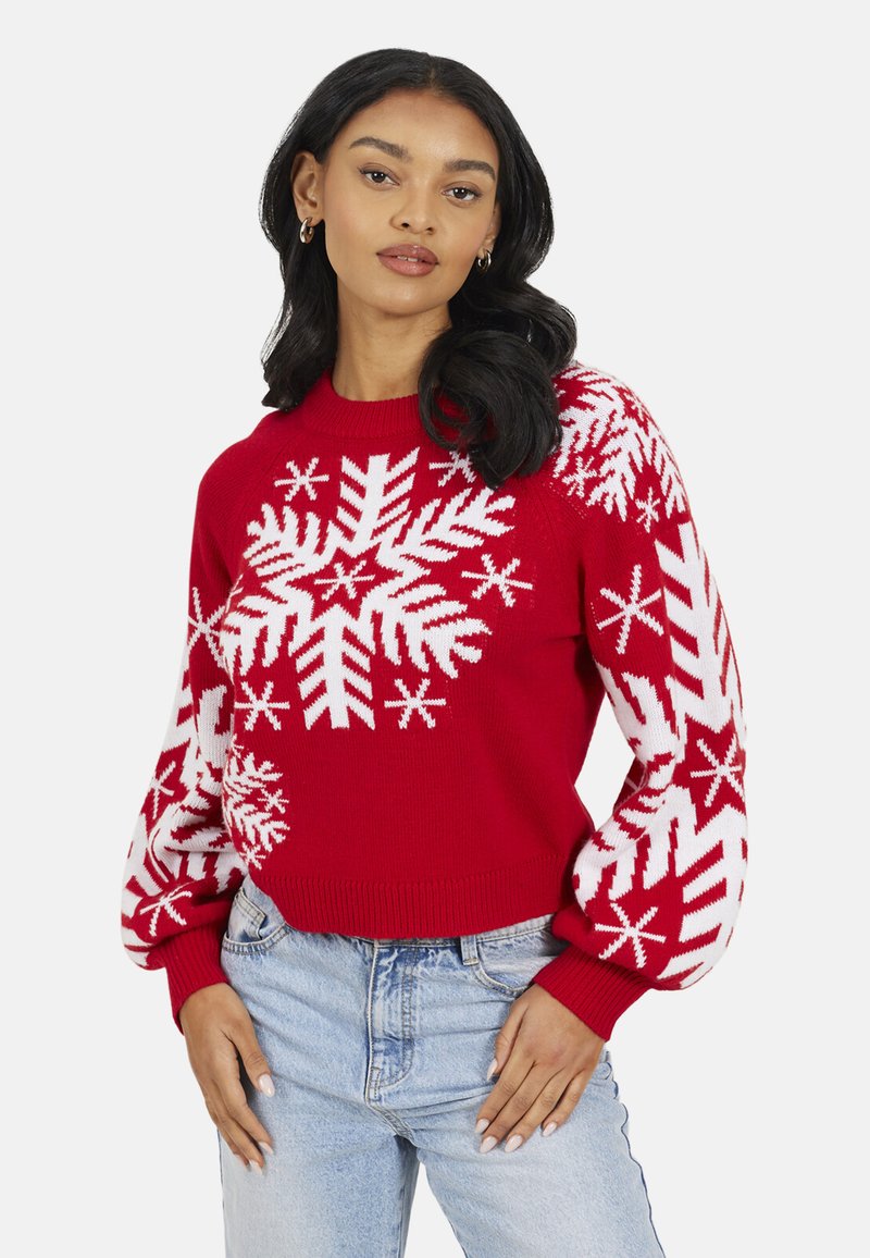 Pull en tricot rouge avec motifs flocons de neige blancs, poignets et ourlet côtelés, coupe décontractée, associé à un jean denim bleu clair.