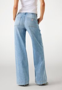 Lichtblauwe denim wijde broek met een hoge taille, voorzien van twee achterzakken en een driehoekige logo patch. Zachte textuur met een ontspannen pasvorm.