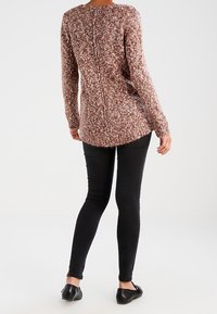 Brązowo-kremowy sweter o fakturze dzianiny z okrągłym dekoltem i długimi rękawami, noszony na czarnych obcisłych jeansach i czarnych balerinach.