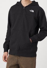 Felpa nera con zip realizzata in tessuto morbido. Presenta una tasca a marsupio e polsini a costine. Piccolo logo bianco sul petto in alto a sinistra.