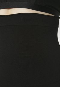 Zwarte hoge taille shapewear met een gladde textuur, voorzien van een subtiel reliëflogo langs de tailleband. Ontworpen voor een nauwsluitende pasvorm.