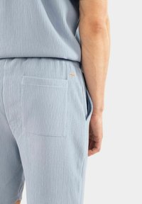 Ljusblå, texturerade shorts i ribbat material, med en bakficka och en liten orange loggdetalj.