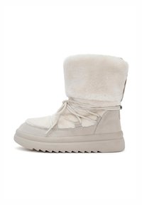 Botas de tobillo beige con un exterior de piel de pelo suave, detalles de ante y una suela de goma texturizada. Presentan cordones y un alto collar de pelo.