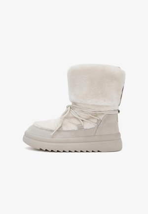 Beige ankle boots with a plush fur upper, suede accents, and a textured rubber sole. Features laces and a tall fur collar.