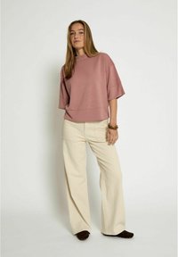 Felpa oversize rosa chiaro con maniche corte, abbinata a pantaloni larghi crema e calzature marroni, con vestibilità comoda e texture morbida.