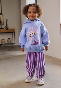 Felpa blu con design floreale, ricamo rosa e vestibilità rilassata. Pantaloni a righe rosa e viola, abbinati a scarpe argento glitterate.