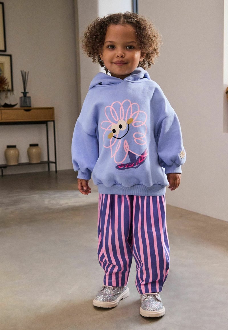 Felpa blu con design floreale, ricamo rosa e vestibilità rilassata. Pantaloni a righe rosa e viola, abbinati a scarpe argento glitterate.