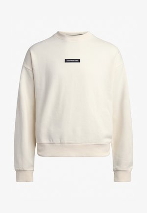 Pulover s krojem crewneck iz kremaste tkanine z mehko teksturo. Vsebuje črn oznako "REDEFINED REBEL" na prsih in rebraste manšete.