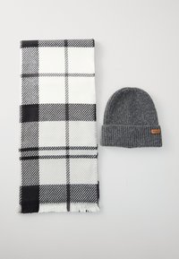 Cachecol xadrez preto e branco com extremidades franjadas, combinado com um gorro de malha cinza escuro, apresentando um pequeno rótulo marrom.