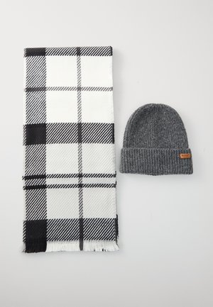 Cachecol xadrez preto e branco com extremidades franjadas, combinado com um gorro de malha cinza escuro, apresentando um pequeno rótulo marrom.