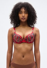 Soutien-gorge imprimé léopard avec accents rouges, doté de bonnets à armatures, bretelles réglables, et d'accessoires dorés décoratifs aux jonctions des bretelles.