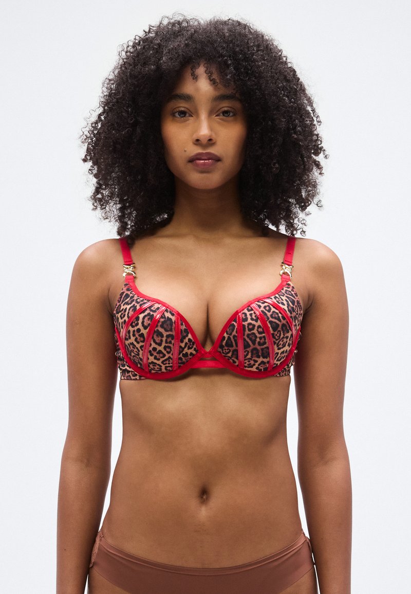 Soutien-gorge imprimé léopard avec accents rouges, doté de bonnets à armatures, bretelles réglables, et d'accessoires dorés décoratifs aux jonctions des bretelles.