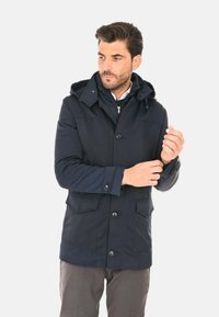 Parka blu navy con cappuccio, dotata di ampie tasche frontali, chiusura con bottoni e texture liscia. Adatta a temperature più fredde.