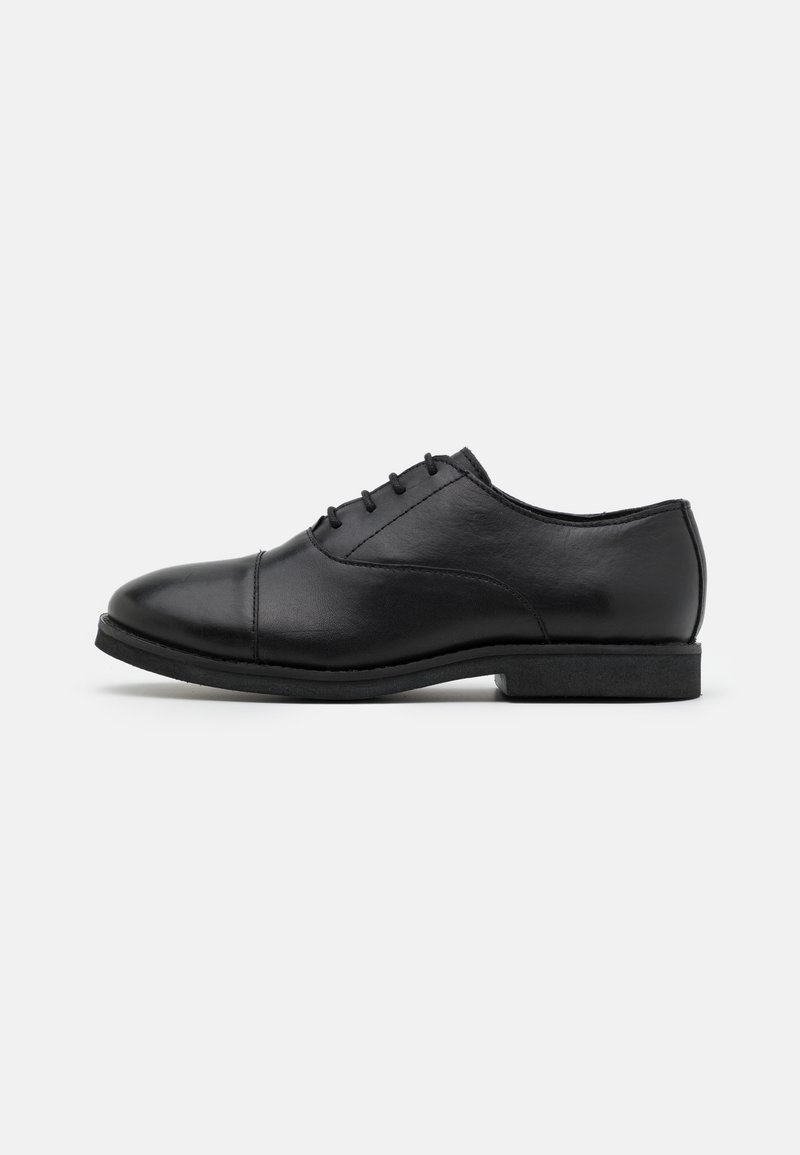 Chaussure habillée noire en cuir avec lacets fermés, petit talon et bout rond, montrée de profil sur fond blanc uni.