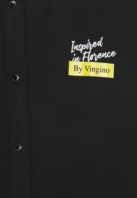 Černá košile s zapínáním na knoflíky, s bílým a žlutým nápisem "Inspired in Florence By Vingino." Hladká textura.