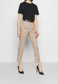 Czarna koszulka z krótkim rękawem w połączeniu z beżowymi spodniami z pionowymi czerwonymi paskami, czarnym paskiem z metalową klamrą oraz czarnymi szpilkami.