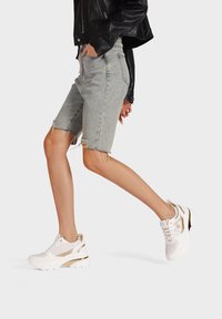 Bermuda shorts in denim scolorito con orli sfrangiati, abbinati a sneaker bianche e dorate con tomaia in rete e suola ammortizzata.