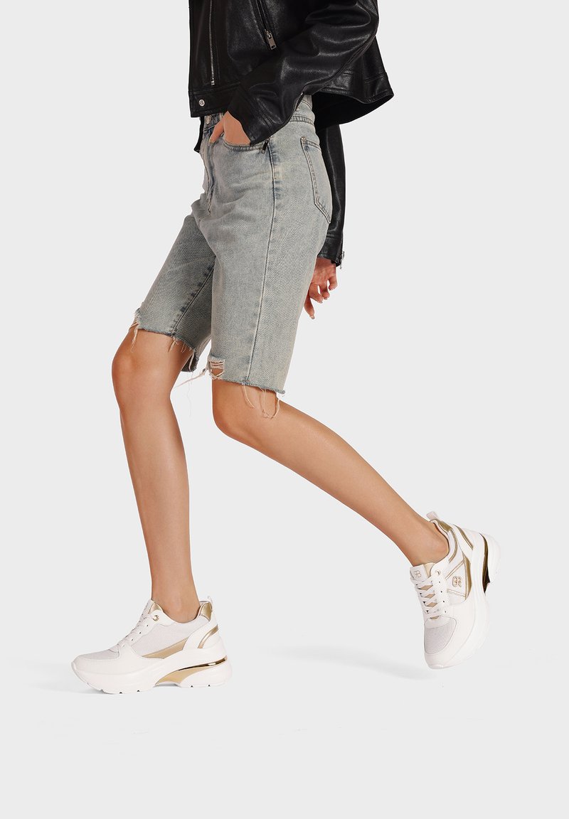 Bermuda shorts in denim scolorito con orli sfrangiati, abbinati a sneaker bianche e dorate con tomaia in rete e suola ammortizzata.