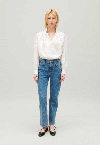 Blusa blanca, holgada, con escote en V y mangas abullonadas, combinada con unos vaqueros azules de pierna recta de talle alto. Bailarinas negras.