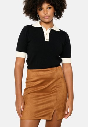 Polo noir à manches courtes avec col et boutons crème associé à une mini jupe en daim beige avec une fente à l'avant. Texture lisse tout au long.