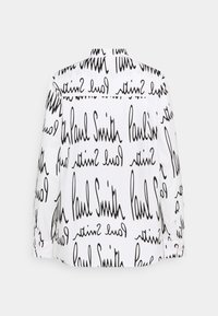 Witte blouse met een herhaald zwart handgeschreven-achtige tekstpatroon met "Paul Smith." Lange mouwen met knoopaccenten bij de manchetten.