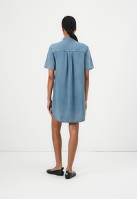 Lys blå denimskjortekjole med korte ermer, krage og rygindsnit, med avrundet kant og svarte flate sko.