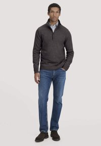 Dunkelgrauer Halbzip-Pullover mit geripptem Saum, getragen über einem weißen Hemd mit Kragen. Kombiniert mit blauen Jeans im geraden Schnitt und dunklen Schuhen.