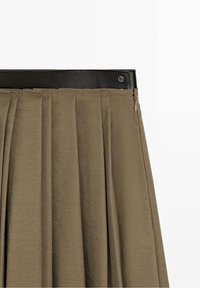 Jupe plissée vert olive avec une ceinture en cuir noire, fermeture éclair latérale et fermeture par bouton pression.