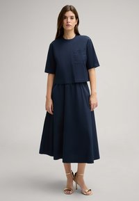 Navy-blaues Zweiteiler-Outfit mit einem kurzen T-Shirt mit kurzen Ärmeln und einer taschenlangen Taillenpartie, kombiniert mit einem schwingenden, knöchellangen Rock.
