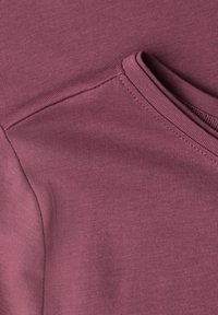 Close-up of a maroon sweatshirt showing the texture and stitching around the shoulder and collar area.