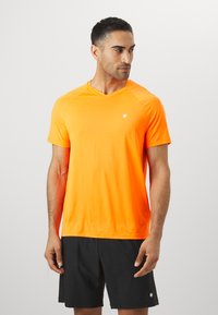 Short-sleeve, v-neck athletic shirt in bright orange, made from lightweight fabric. Features a small white logo on the chest.