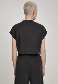 Fekete, rövid ujjú, cropped póló, puha anyagból készült, kerek nyakkivágással és egyenes szegéllyel. Egyszerű és minimalista dizájn.