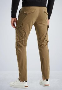 Khaki cargo hlače z več stranskimi žepi, prilagojenim dizajnom in zoženimi nogami, izdelane iz teksturiranega bombaža. Nosi se z belimi supergami.