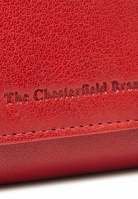 Portafoglio in pelle rossa con finitura testurizzata. Presenta bordi cuciti e testo impresso che legge "The Chesterfield Brand."