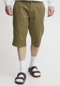 Khaki színű cargo sort oldalpanel részletekkel, pamut anyagból, varrott díszítéssel és laza szabással. Fehér zoknikkal és barna szandálokkal párosítva.