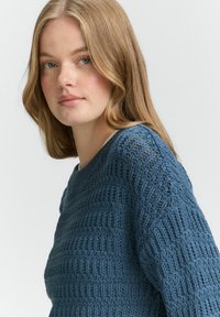 Maglione blu lavorato a maglia con un motivo testurizzato, scollatura rotonda e maniche lunghe. Il materiale presenta un design a trama aperta e morbida.