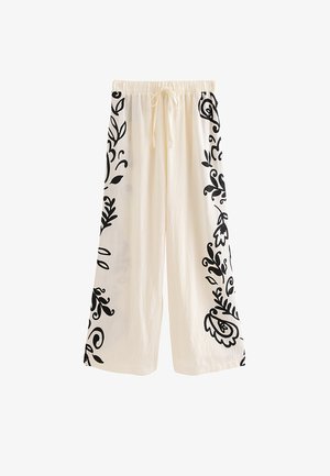 Pantalones blancos de pierna ancha con estampados florales negros a lo largo de los lados exteriores y una cintura elástica con cordón delantero.