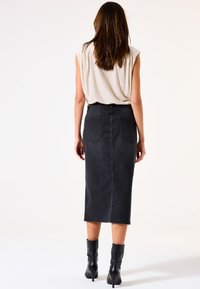 Schwarzer Denim-Midirock mit mittelhoher Taille, zwei Gesäßtaschen und einer glatten Textur, kombiniert mit schwarzen Ankle Boots.