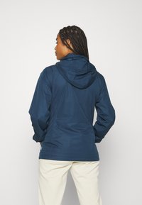 Marinblå vattentät jacka med huva, som har en lätt design och en slät yta, sedd bakifrån. Inga synliga mönster eller detaljer.
