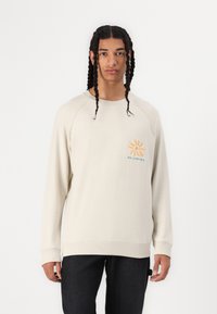 Hellbeige Sweatshirt mit Raglanärmeln, ausgestattet mit einem orangefarbenen Sonnendesign und türkisfarbenem Text. Weiches Baumwollmaterial mit eng anliegenden Bündchen und Saum.