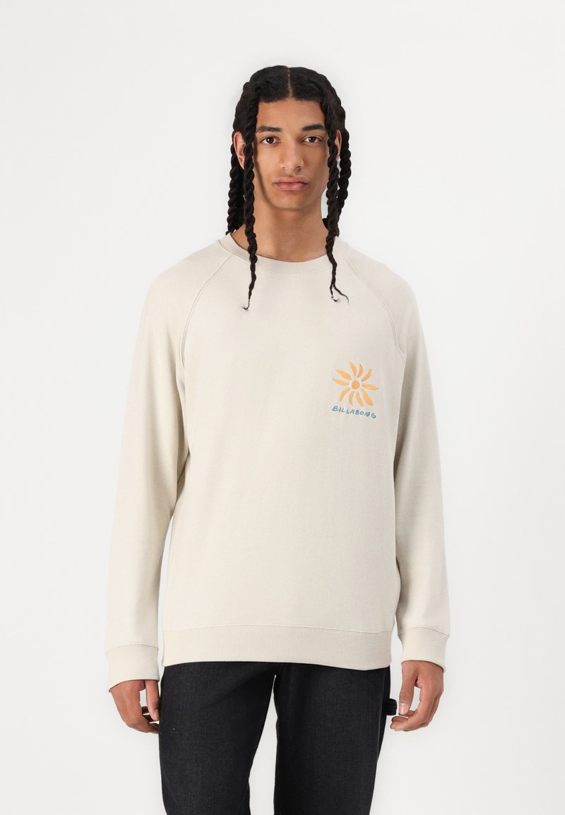 Hellbeige Sweatshirt mit Raglanärmeln, ausgestattet mit einem orangefarbenen Sonnendesign und türkisfarbenem Text. Weiches Baumwollmaterial mit eng anliegenden Bündchen und Saum.