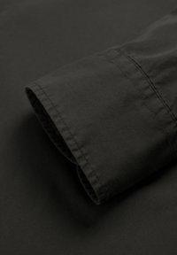 Manga de tela negra plegada con detalles de costura visibles sobre una superficie oscura, resaltando la textura y la calidad del material.