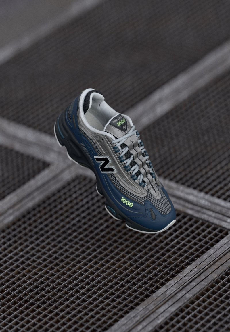 Baskets New Balance 1000 bleu marine et gris avec des détails réfléchissants posées sur un fond de grille métallique.