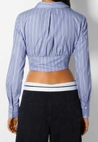 Avklippt, långärmad skjorta i ljusblått med vita och marinblå vertikala ränder, med sjalkrage och sammangatherad ryggdesign.