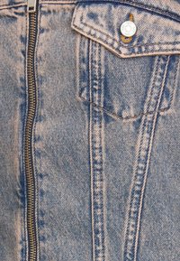 Jeansjacka i ljusblå färg, silverdragkedja och koppardetaljer. Har bröstfickor, kontrastsömmar och textilmaterial med struktur.